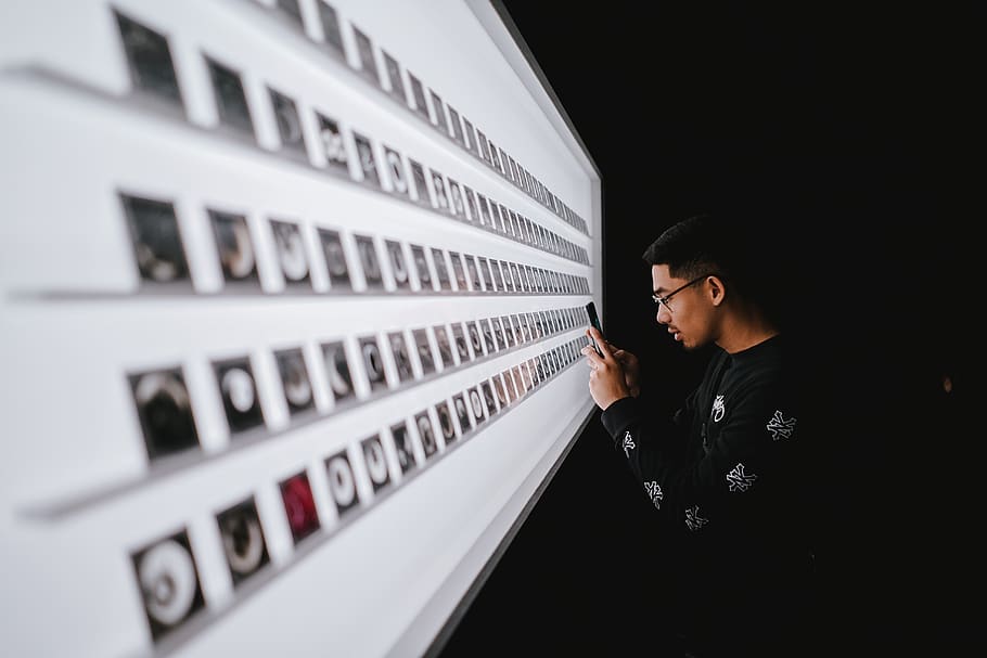 stående, mand, ved brug af, smartphone, ord, person, human, tekst, ansigt, frakke, overfrakke, beklædning, tøj, alfabet, symbol, hoved, nummer, langærmet, ærme, elektronik, tastatur, privat postkasse, postkontor, finger, en person, briller, voksen, herrer, indendørs, livsstil, leder, fritidsaktivitet, ung voksen, meddelelse, midt voksen, hovedskud, portræt, rigtige mennesker, teknologi, offentliggørelse, forretning, søger, overvejelse, 5K